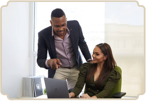 A guy pointing at a laptop screen next to a woman by her desk